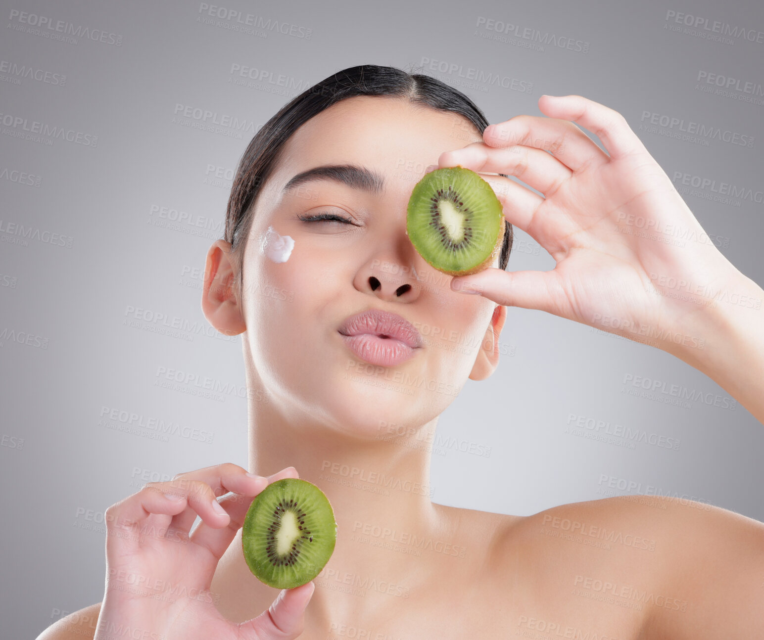 Buy stock photo Studio shot of an attractive young woman posing with two halves of a kiwi against a grey background