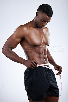 Buy stock photo Studio shot of a handsome young musclar man measuring his waist against a grey background