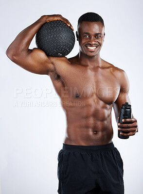 Buy stock photo Studio portrait of a handsome young muscular man posing with a medicine ball and water bottle against a grey background