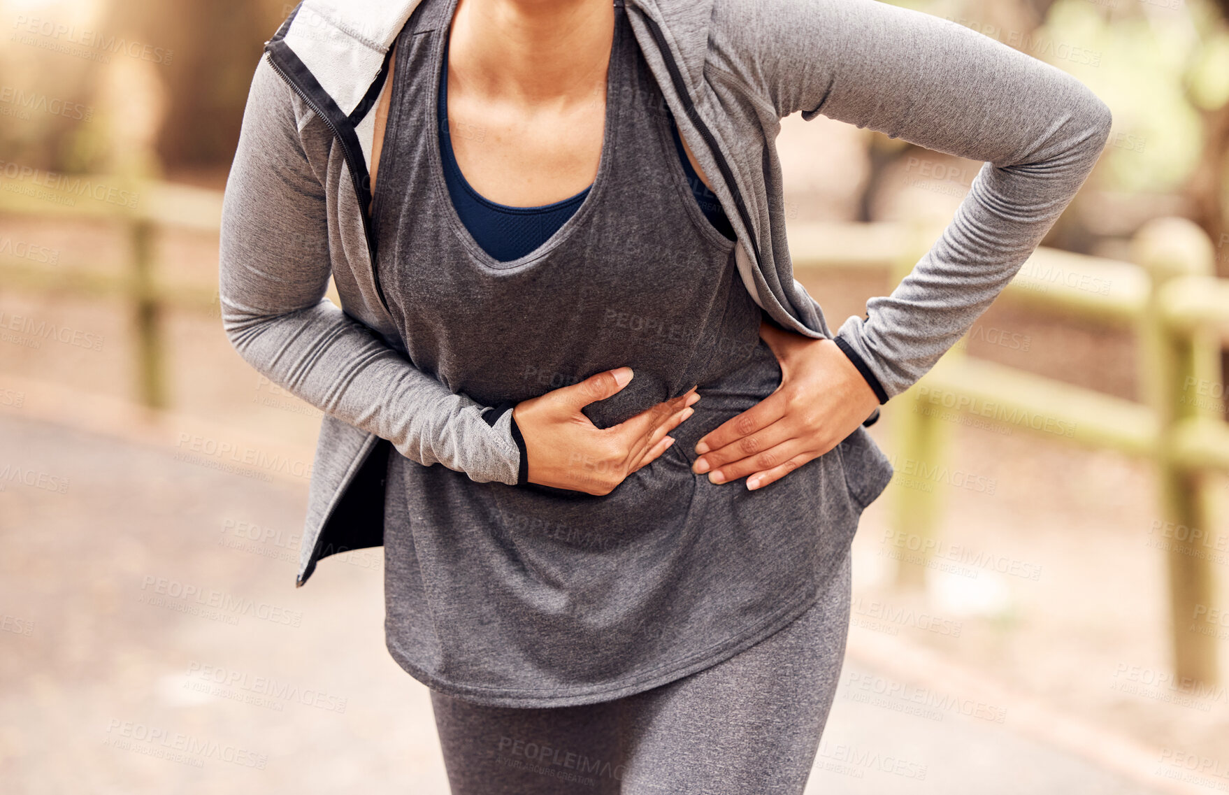 Buy stock photo Shot of an unrecognisable woman experiencing stomach ache while working out in nature