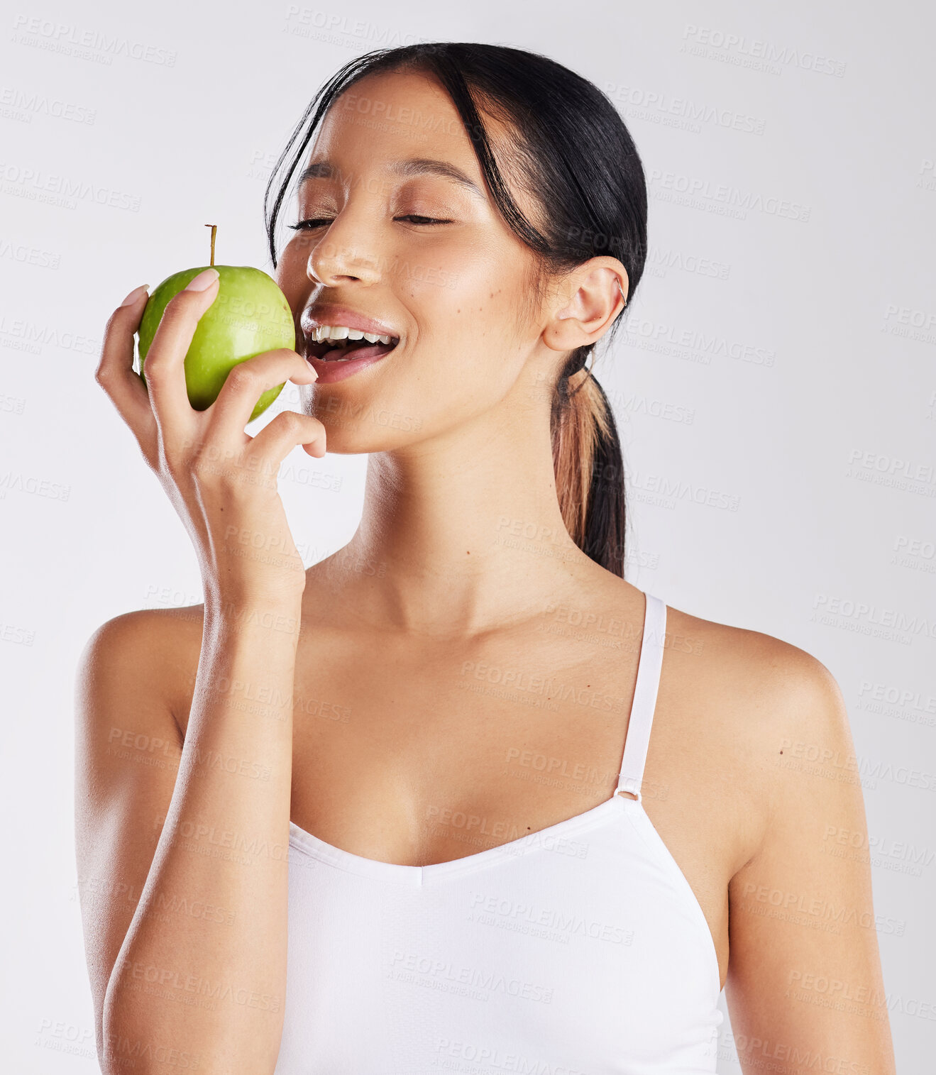 Buy stock photo Shot of a healthy young woman holding an apple while posing against a studio background