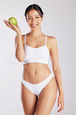 Buy stock photo Shot of a healthy young woman holding an apple while posing against a studio background