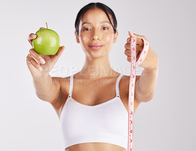Buy stock photo Shot of a healthy young woman holding an apple and a measuring tape