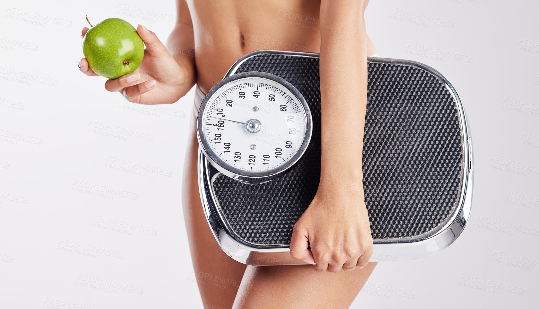 Buy stock photo Shot of a healthy young woman holding an apple and a weight scale