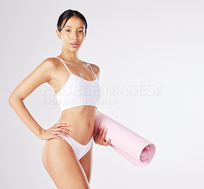 Buy stock photo Shot of a fit young woman holding a yoga mat while standing against a studio background