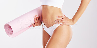 Buy stock photo Shot of a fit young woman holding a yoga mat while standing against a studio background