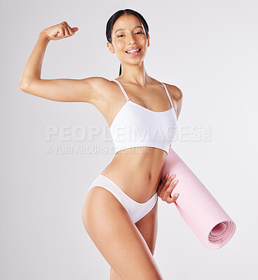 Buy stock photo Shot of a fit young woman holding a yoga mat while standing against a studio background