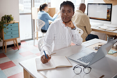 Buy stock photo Shot of a young businesswoman using a laptop and writing in a notebook in a modern office