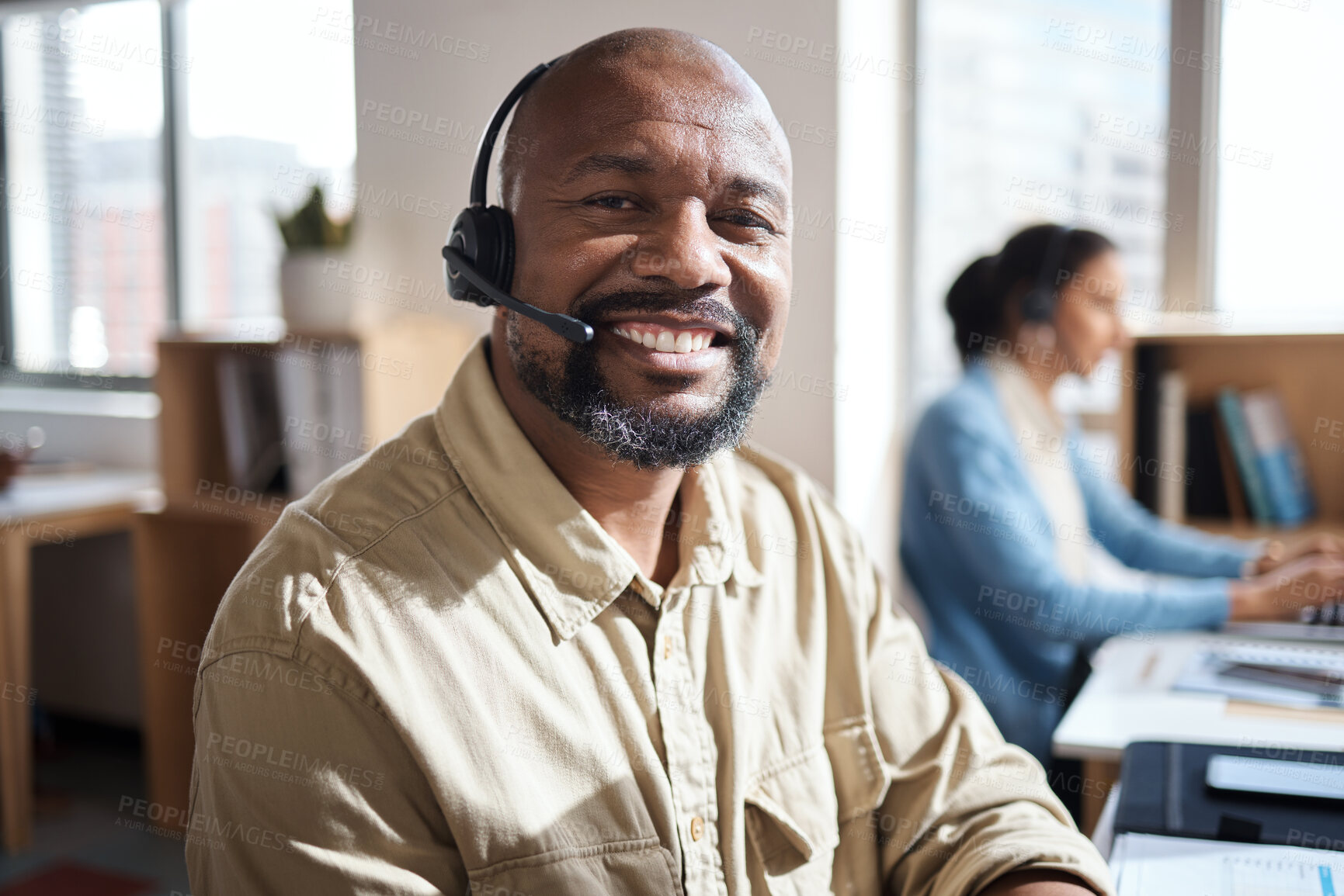 Buy stock photo Shot of a mature businessman using a headset in a modern office with his colleague working in the background