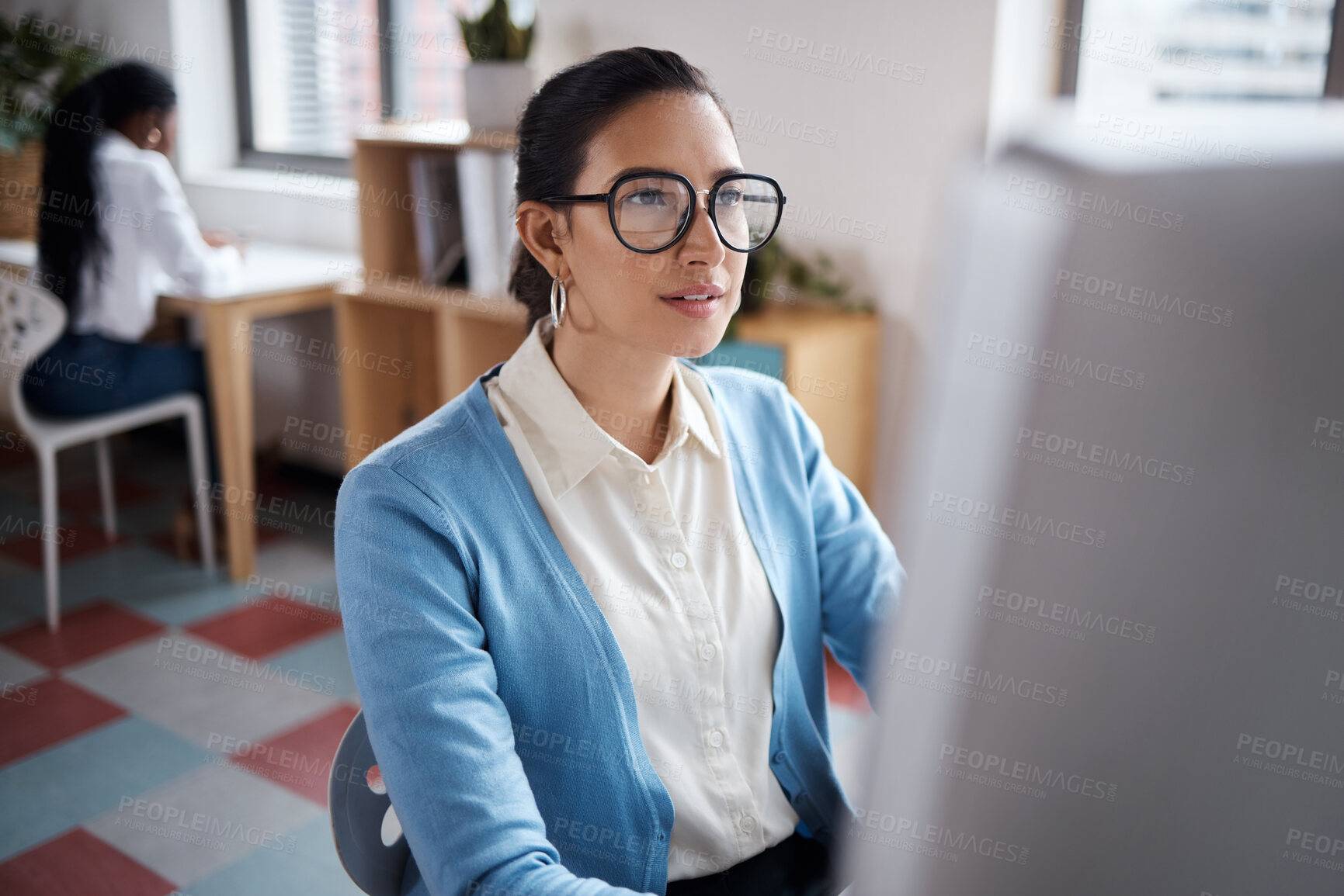 Buy stock photo Shot of a young businesswoman using a computer at her desk in a modern office