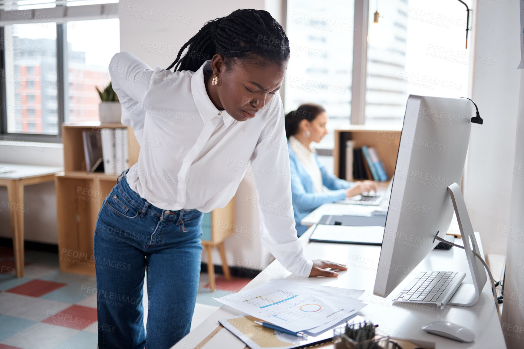 Buy stock photo Shot of a young businesswoman experiencing back pain while working at her desk in a modern office