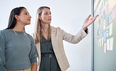 Buy stock photo Shot of two businesswomen brainstorming with sticky notes on a chalkboard