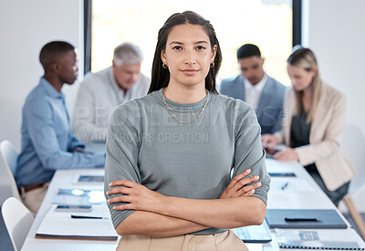 Buy stock photo Portrait of a confident young businesswoman standing with her arms crossed in an office while her colleagues have a meeting in the background