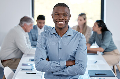 Buy stock photo Portrait of a confident young businessman standing with his arms crossed in an office while his colleagues have a meeting in the background