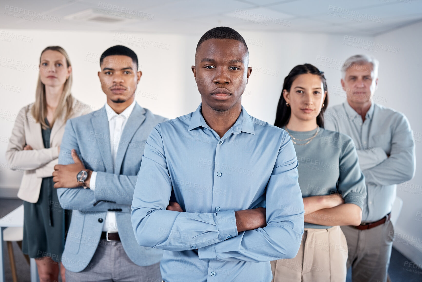 Buy stock photo Portrait of a confident young businessman standing with his arms crossed in an office with his colleagues behind him