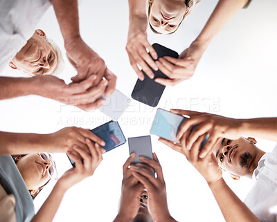 Buy stock photo Low angle shot of a group of unrecognisable businesspeople using their smartphones in a modern office