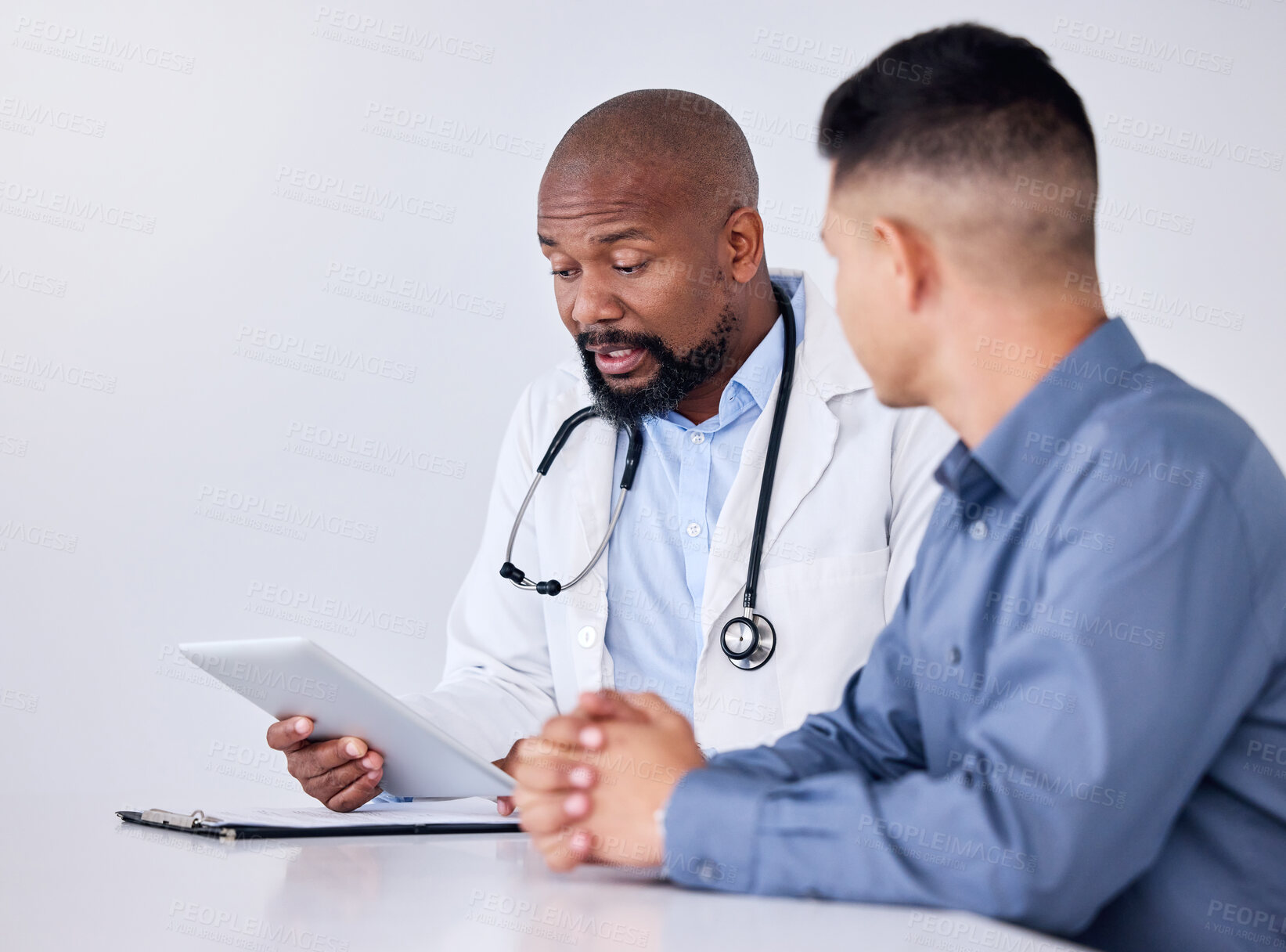 Buy stock photo Shot of a mature male doctor using a digital tablet during a consultation at a clinic