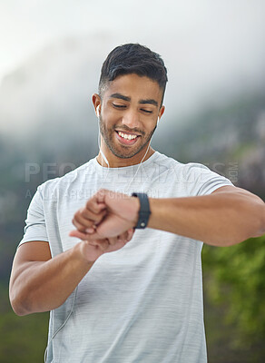 Buy stock photo Shot of a sporty young man wearing earphones and checking his watch while exercising outdoors
