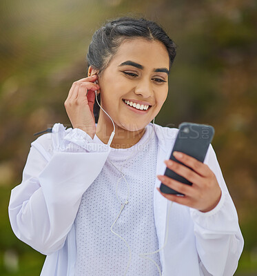 Buy stock photo Shot of a sporty young woman wearing earphones and using a cellphone while exercising outdoors