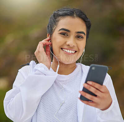 Buy stock photo Portrait of a sporty young woman wearing earphones and using a cellphone while exercising outdoors