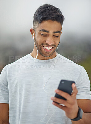 Buy stock photo Shot of a sporty young man wearing earphones and using a cellphone while exercising outdoors