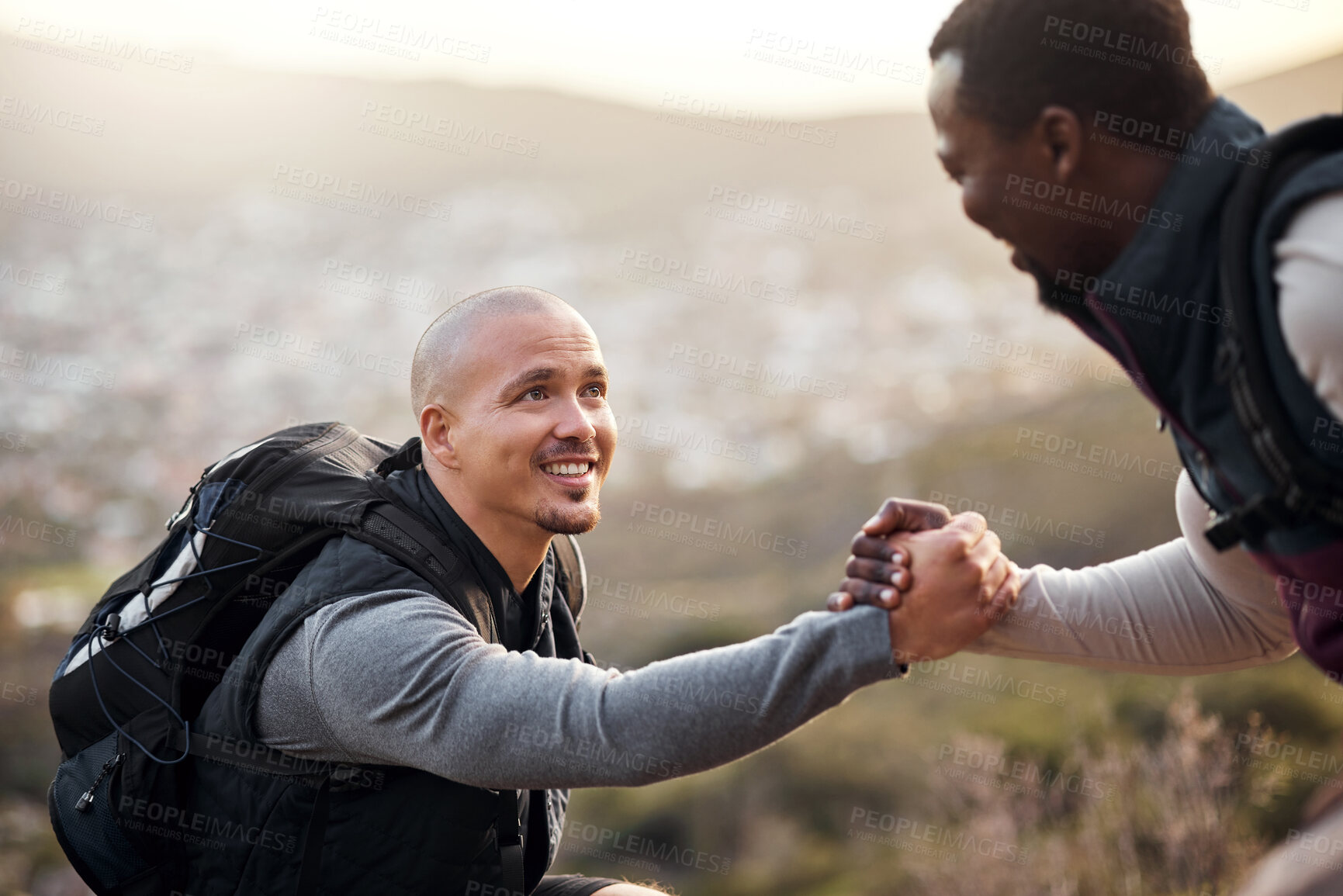 Buy stock photo Cropped shot of a handsome young man helping his friend along a mountain during their hike