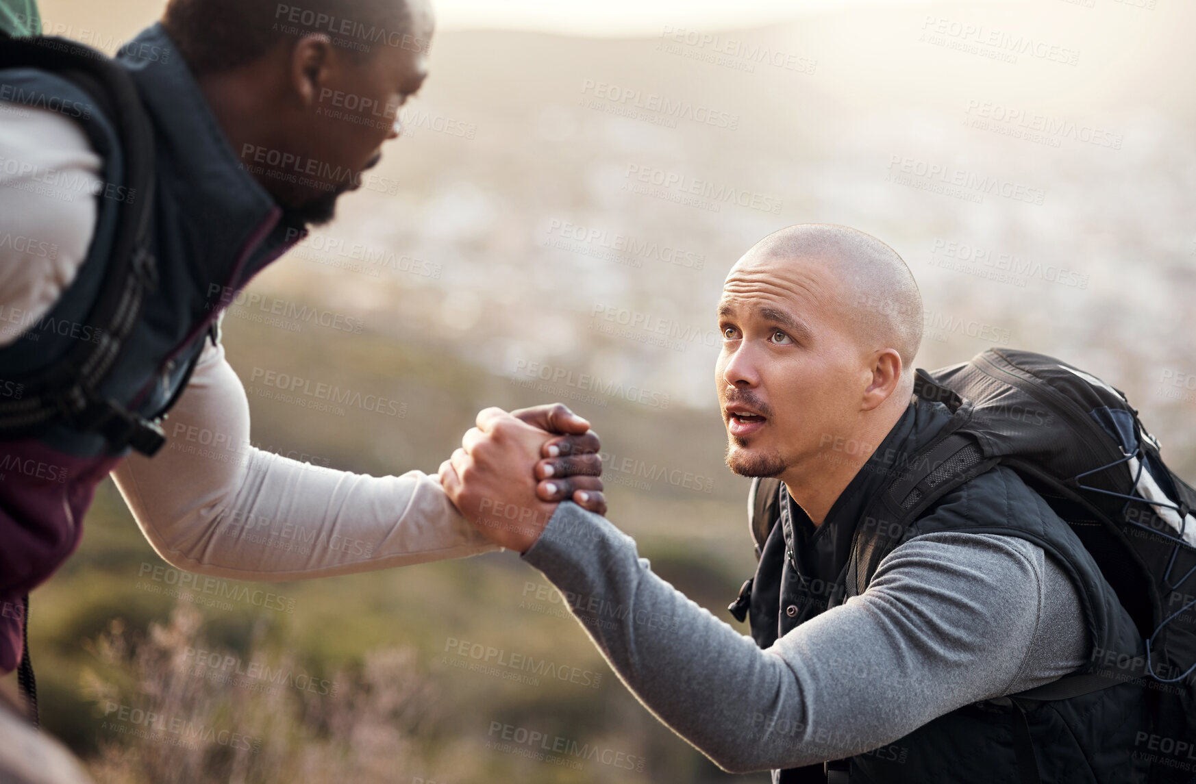 Buy stock photo Cropped shot of a handsome young man helping his friend along a mountain during their hike