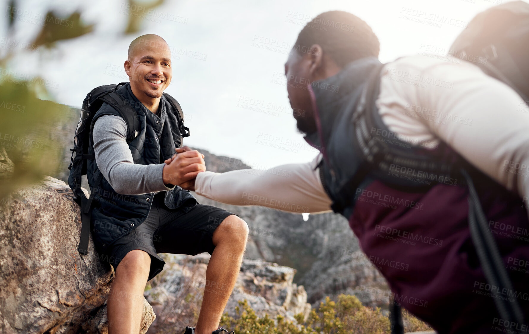 Buy stock photo Cropped shot of a handsome young man helping his friend along a mountain during their hike