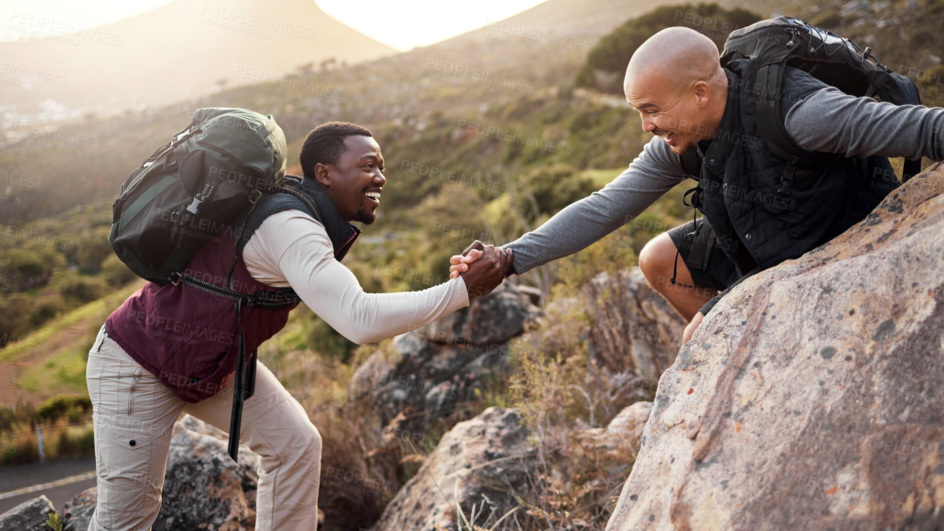 Buy stock photo Cropped shot of a handsome young man helping his friend along a mountain during their hike