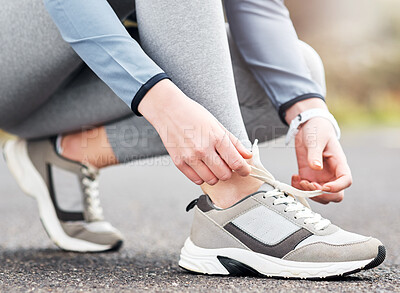 Buy stock photo Cropped shot of a woman tying her shoelaces while out for a run on a road
