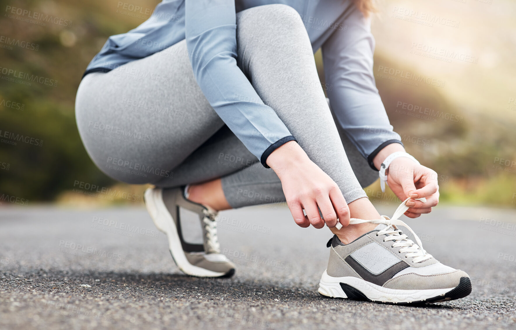 Buy stock photo Cropped shot of a woman tying her shoelaces while out for a run on a road