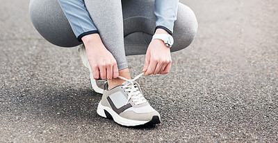 Buy stock photo Cropped shot of a woman tying her shoelaces while out for a run on a road