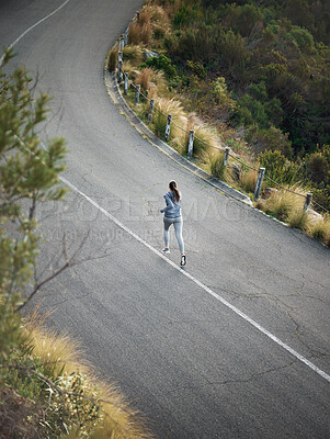 Buy stock photo High angle shot of a woman out for a run on a mountain road