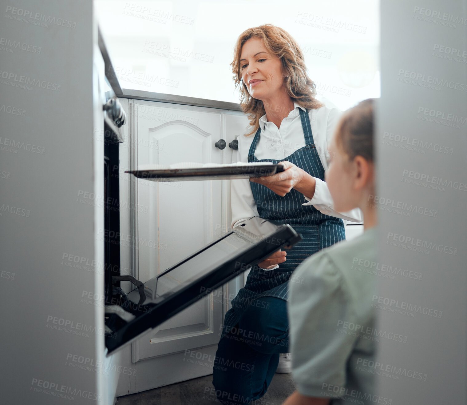 Buy stock photo Shot of a grandmother inserting a tray into a hot oven while baking with her granddaughter at home