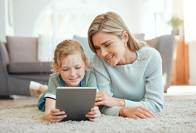 Buy stock photo Shot of an attractive young woman lying on the living room floor with her daughter and using a digital tablet