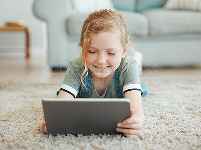 Buy stock photo Shot of an adorable little girl lying alone on the living room floor and using a digital tablet