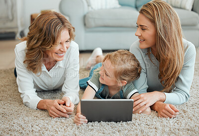 Buy stock photo Shot of a little girl lying on the living room floor with her mother and grandmother while using a digital tablet