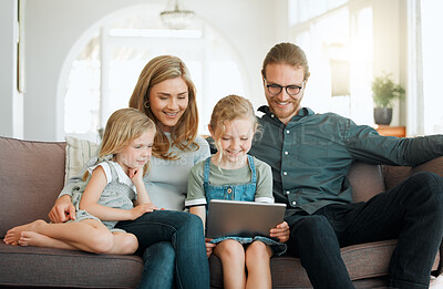 Buy stock photo Shot of a young family sitting on the sofa together and bonding while using a digital tablet