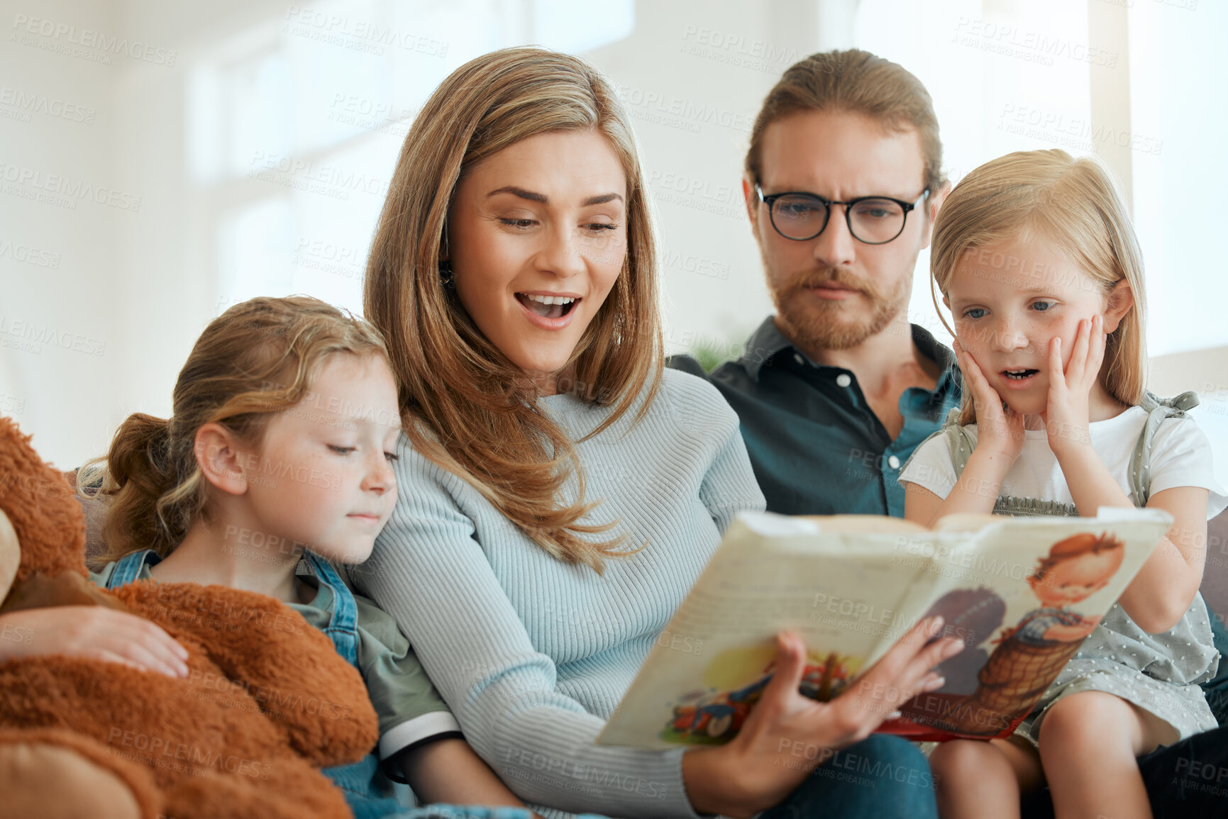 Buy stock photo Shot of an attractive young woman sitting with her family on the sofa at home and reading a book