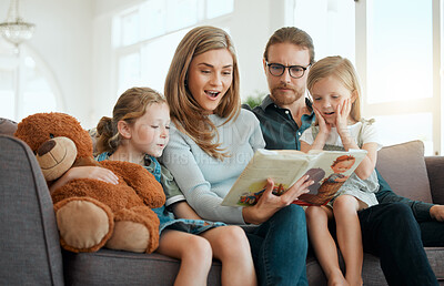Buy stock photo Shot of an attractive young woman sitting with her family on the sofa at home and reading a book
