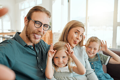 Buy stock photo Shot of a young family sitting on the sofa at home and taking a silly selfie