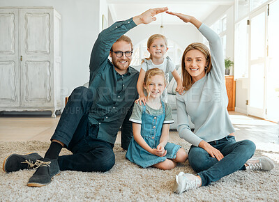 Buy stock photo Full length shot of a young couple sitting on the living room floor and making a home gesture over their daughters