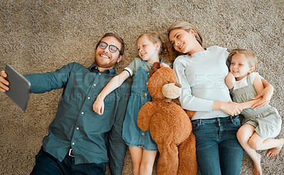 Buy stock photo High angle shot of a young family lying on the living room floor and using a digital tablet