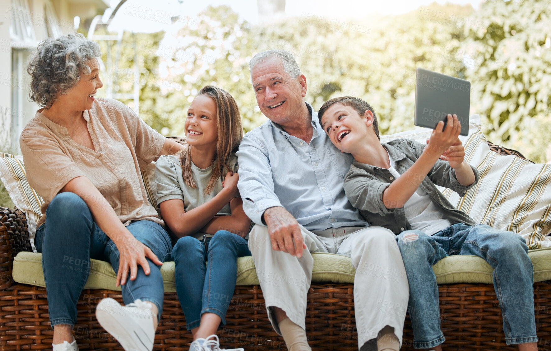 Buy stock photo Shot of a young boy using a digital tablet while sitting at home with his sister and grandparents