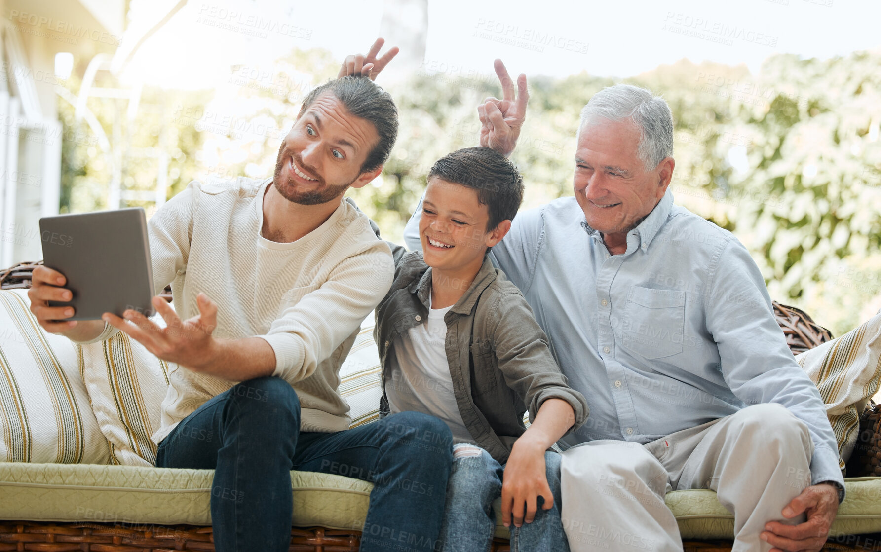 Buy stock photo Shot of a man using a digital tablet while sitting outside with son and his elderly father
