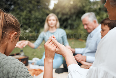 Buy stock photo Shot of a multi-generational family praying together while having a picnic outside