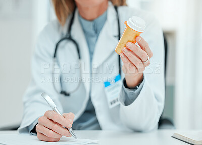 Buy stock photo Cropped shot of an unrecognisable doctor sitting alone in her clinic and writing notes while holding a bottle of pills