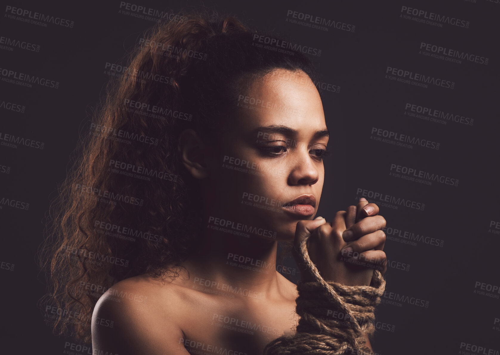 Buy stock photo Frustrated woman, hands and tie with rope for kidnapping, hostage or slavery on a dark studio background. Young, female person or victim with binding in fear for human trafficking, trauma or abuse