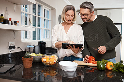 Buy stock photo Shot of a mature couple using a digital tablet while cooking together at home