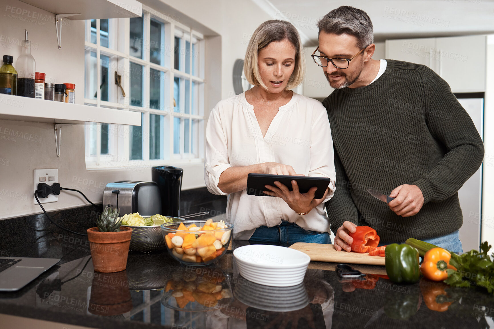 Buy stock photo Shot of a mature couple using a digital tablet while cooking together at home